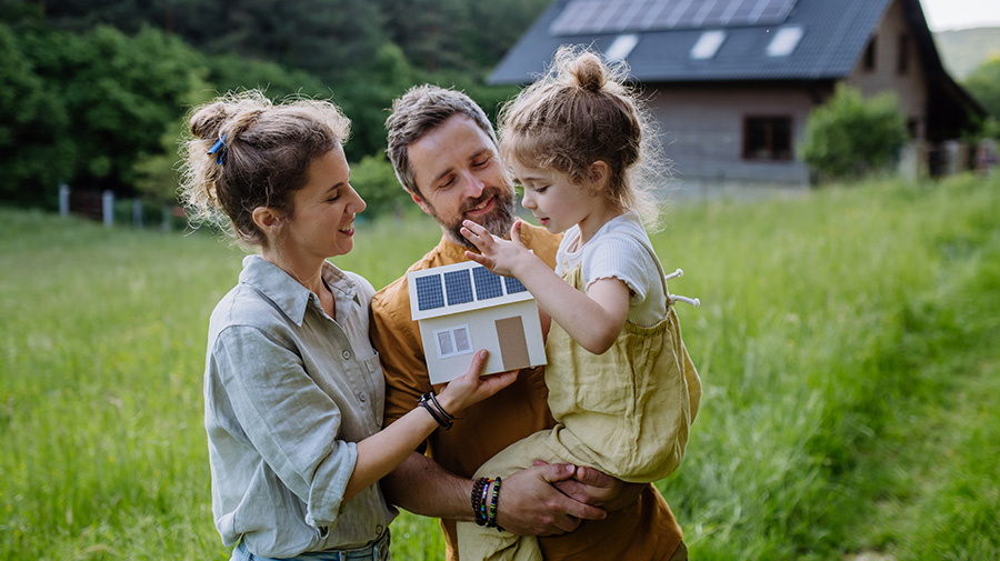 Family in field holding doll house with solar panels